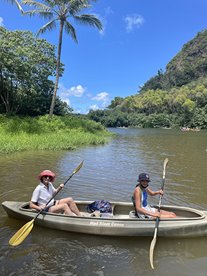Person paddling canoe on calm river palm trees
